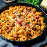 A close-up view of a black bowl filled with creamy pasta, meatballs, diced tomatoes, and grated cheese, garnished with parsley.