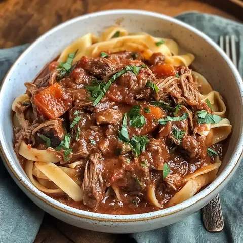 A bowl of fettuccine pasta topped with a rich savory meat sauce, featuring shredded beef and diced carrots, garnished with fresh herbs.