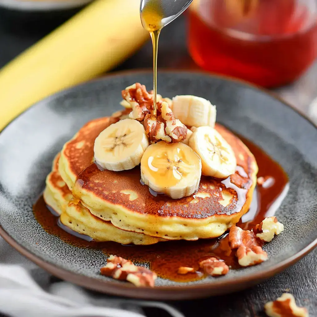 A plate of three fluffy pancakes topped with sliced bananas, chopped walnuts, and a drizzle of syrup.