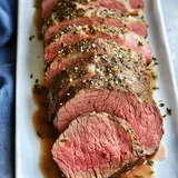 A platter of expertly sliced roast beef, seasoned with herbs and garnished with salt, served in a savory sauce.