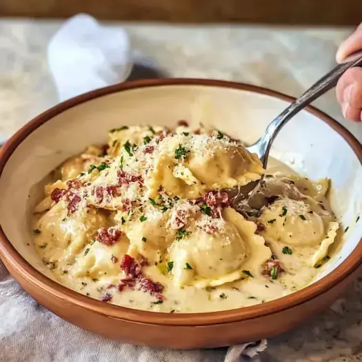 A bowl of creamy ravioli topped with bacon bits and parsley, with a fork scooping some out.