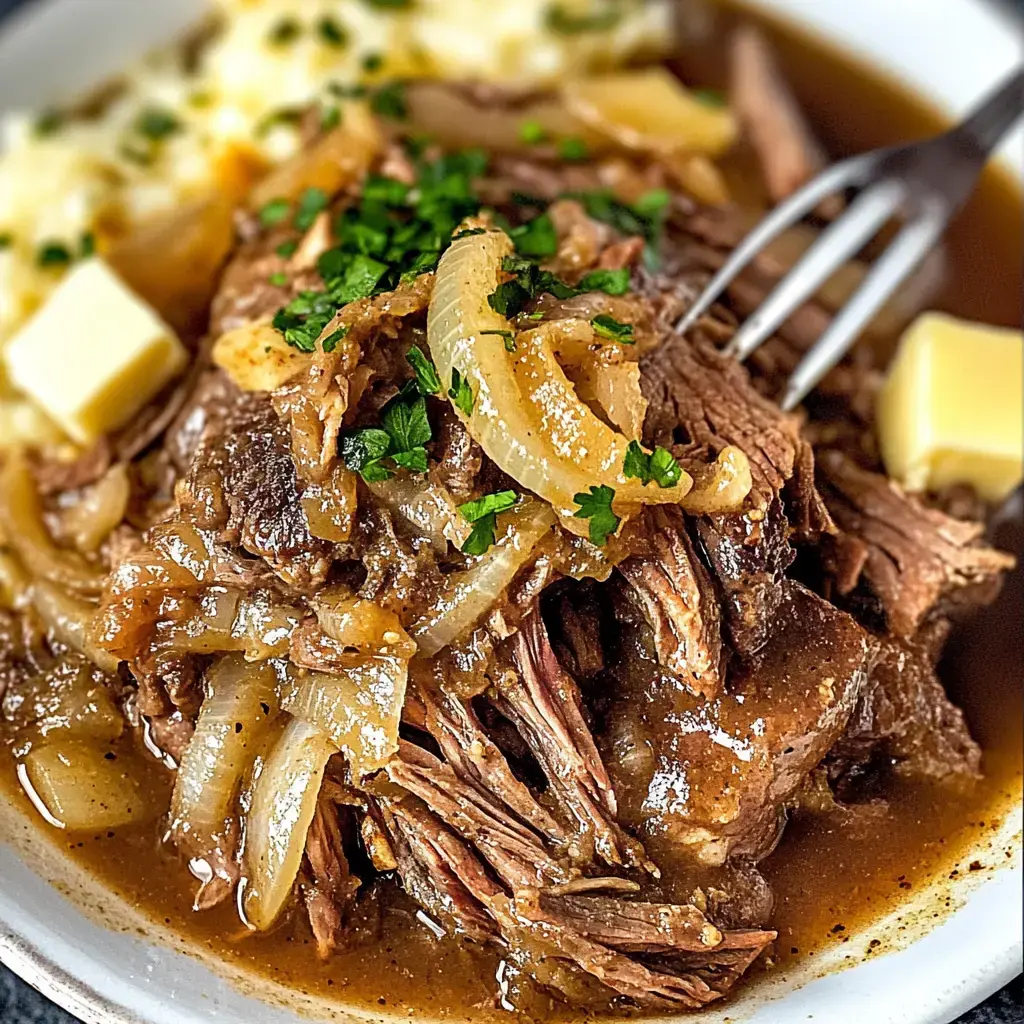 A close-up of savory, shredded beef with onions and herbs, served with mashed potatoes and butter on a white plate.