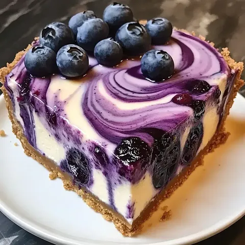 A slice of blueberry cheesecake with a creamy purple swirl and fresh blueberries on top, served on a white plate.