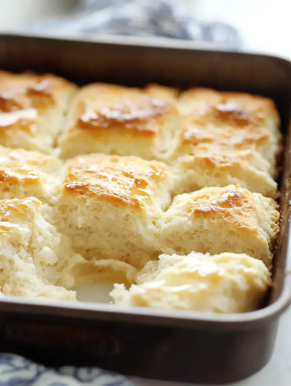 A freshly baked tray of golden-brown biscuits with a few pieces pulled apart, revealing their fluffy interior.