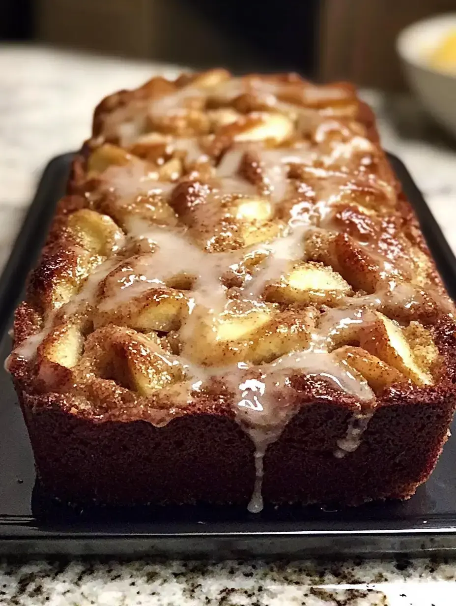 A freshly baked cake topped with a glaze and pieces of apple, presented on a dark serving tray.