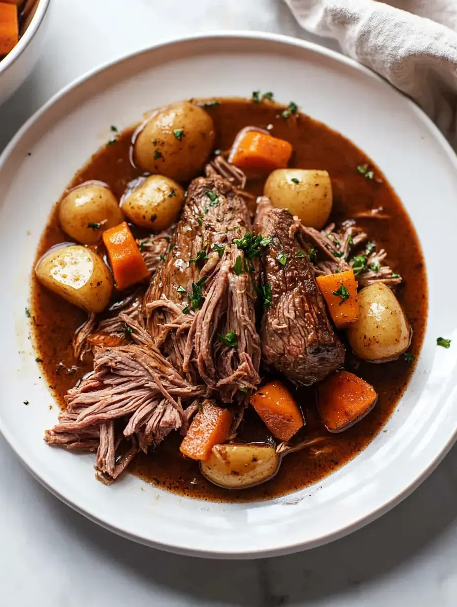 A plate of tender, shredded beef surrounded by baby potatoes, carrots, and broth, garnished with chopped parsley.