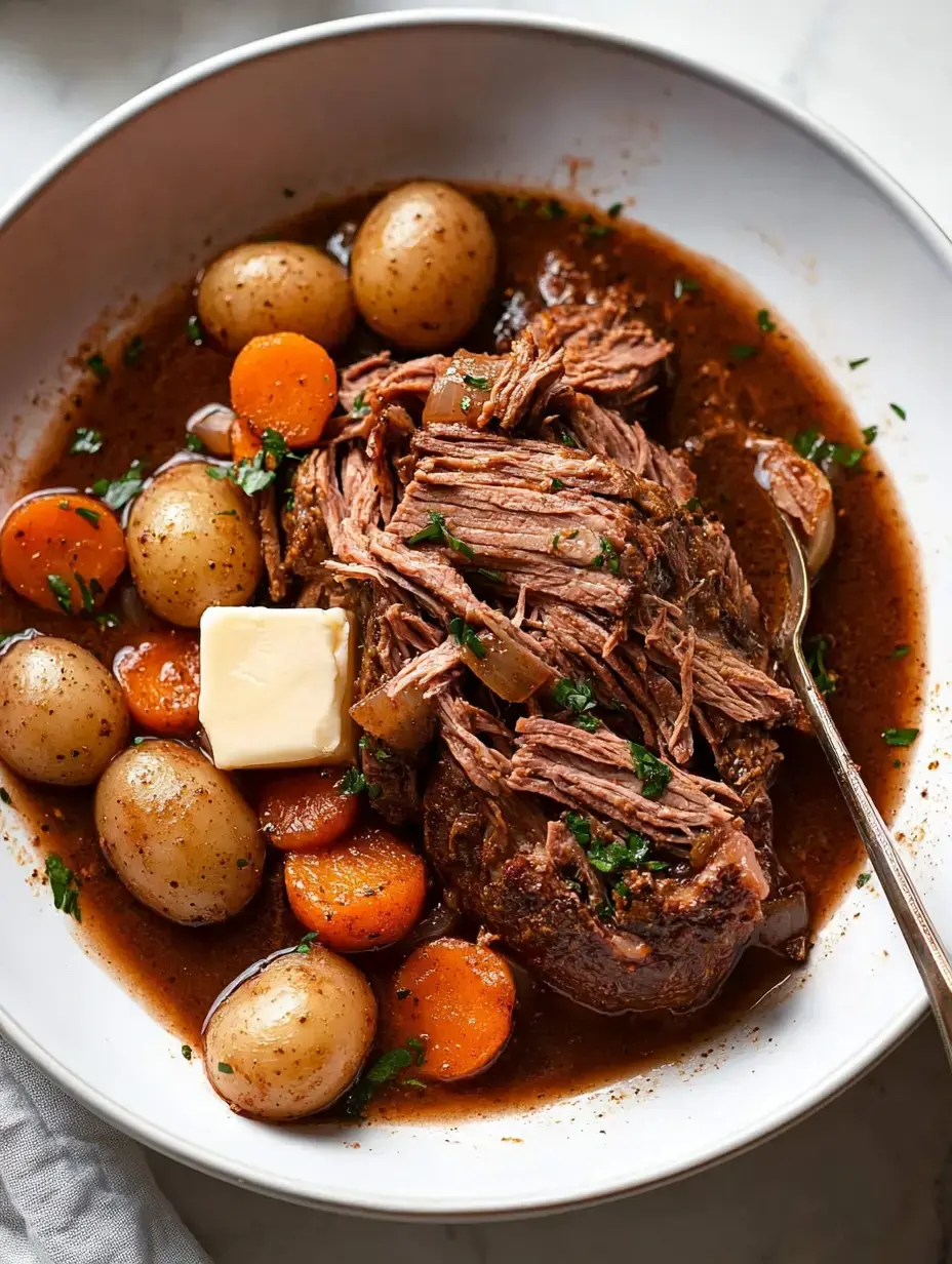 A serving of tender shredded beef with baby potatoes and carrots, topped with a pat of butter and garnished with parsley in a white bowl.