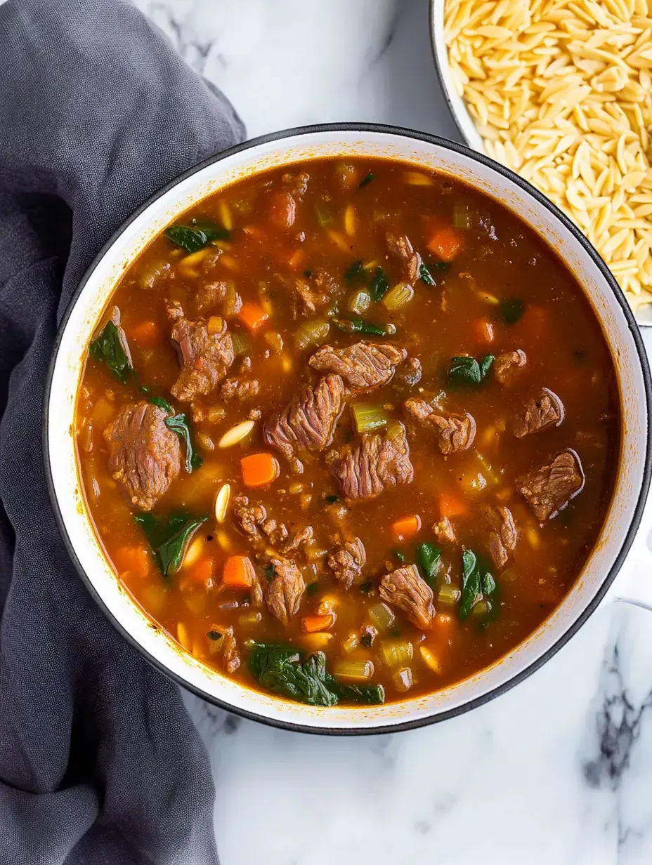 A bowl of hearty beef and vegetable soup with spinach and carrots, accompanied by a side of orzo pasta.