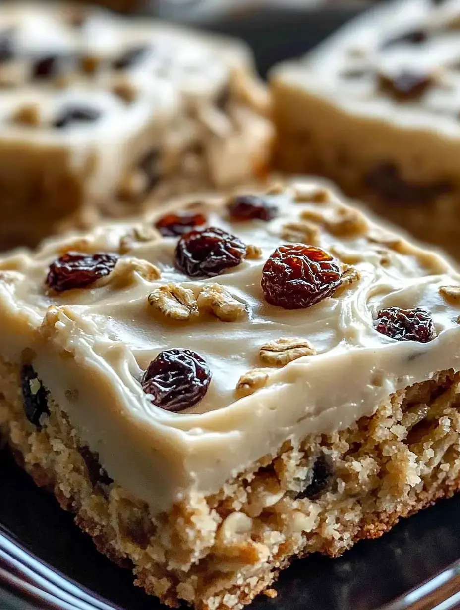 A close-up view of a slice of dessert topped with creamy frosting, raisins, and oats on a dark plate.