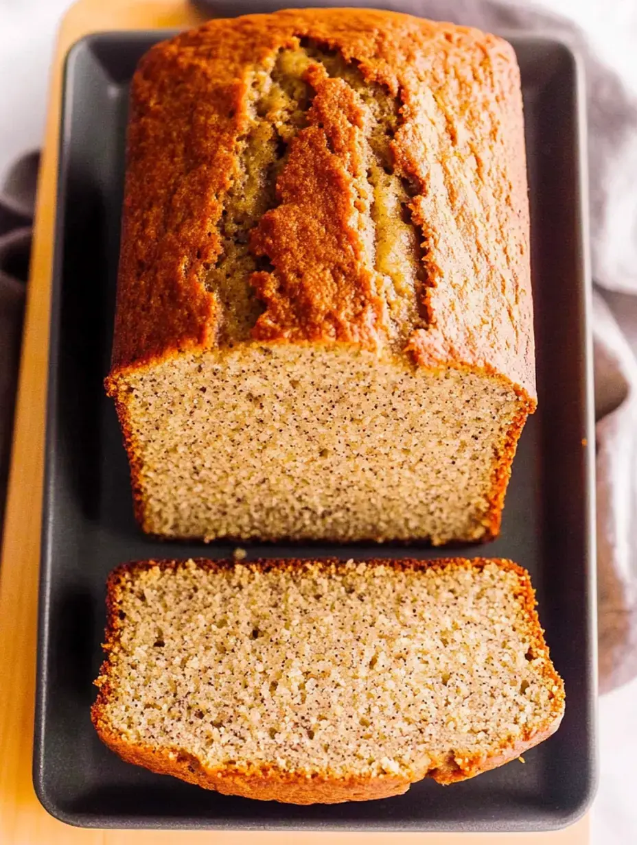 A freshly baked loaf of bread is placed on a dark plate, with a slice cut and positioned next to the whole loaf.