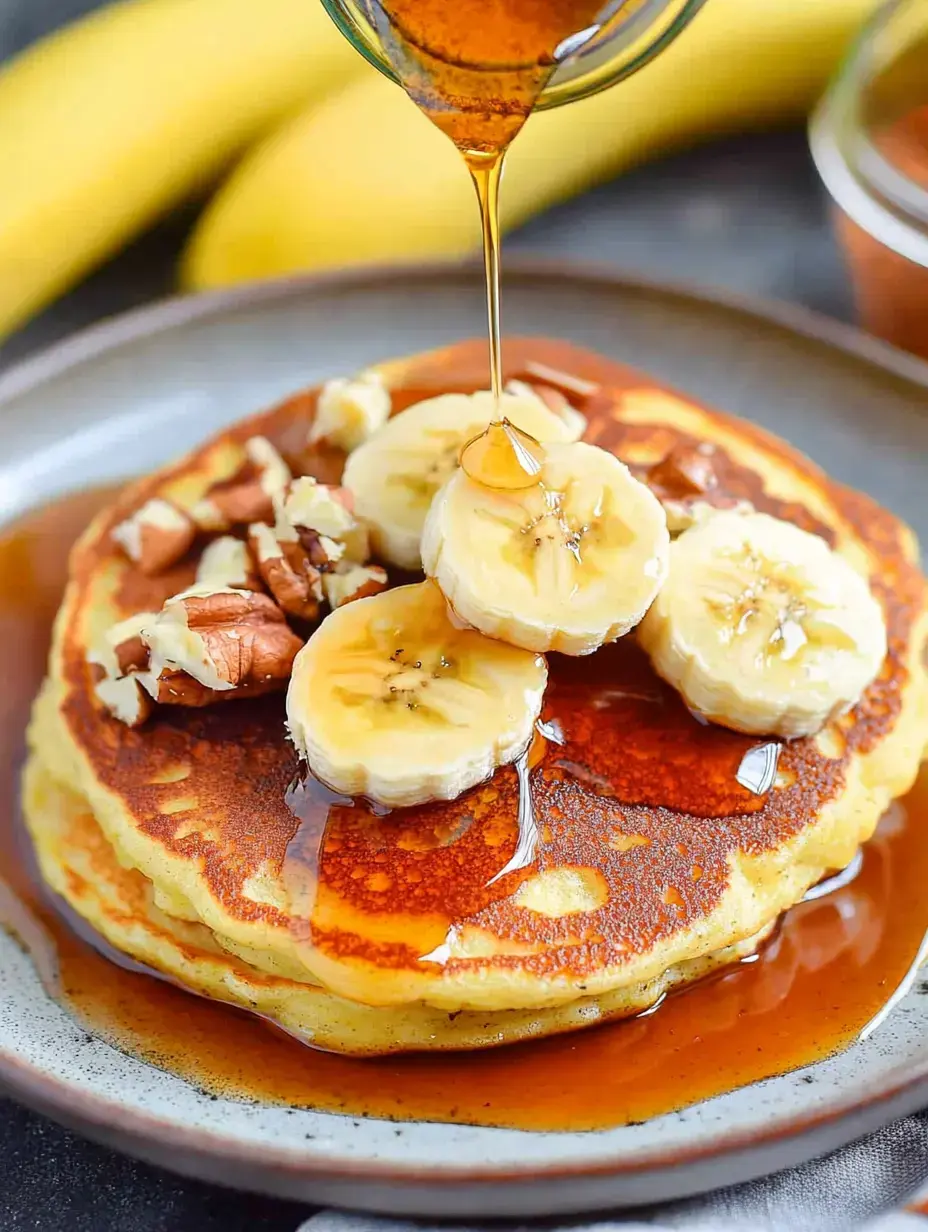 A stack of pancakes topped with sliced bananas, nuts, and drizzled with syrup on a plate.