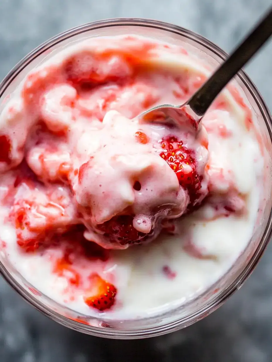 A close-up of a bowl filled with creamy yogurt mixed with fresh strawberries and a spoon resting inside.