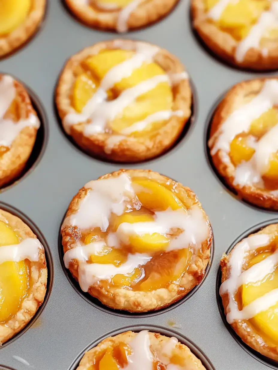 A close-up of mini fruit tarts with peach slices and a drizzle of icing, arranged in a muffin tin.