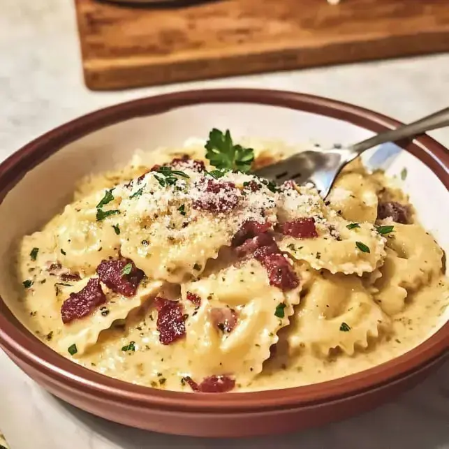 A bowl of creamy pasta topped with crispy bacon bits, grated cheese, and fresh parsley.