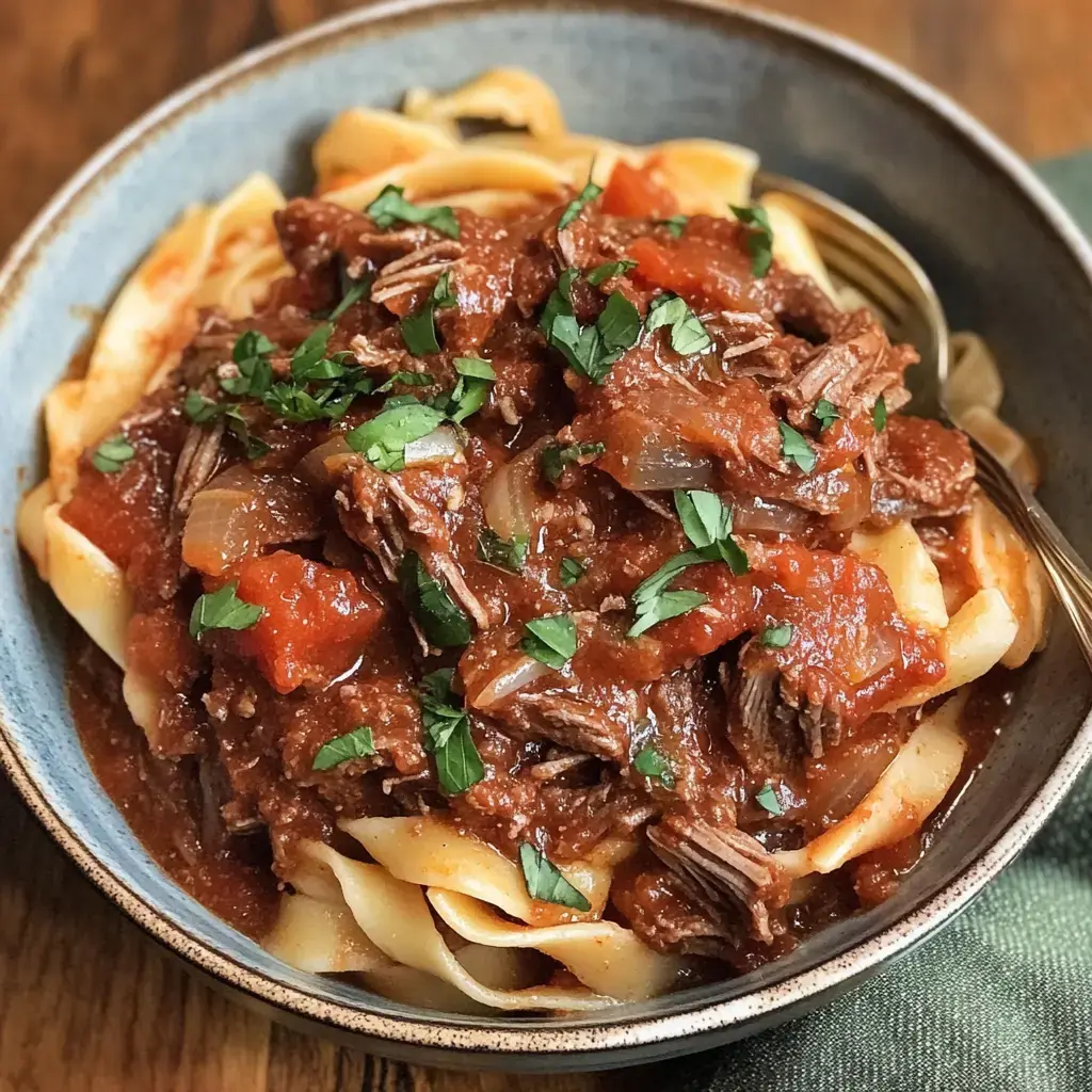 A bowl of pasta topped with a rich beef and tomato sauce, garnished with fresh parsley.