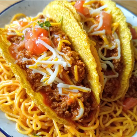 A plate of food with two tacos and spaghetti.