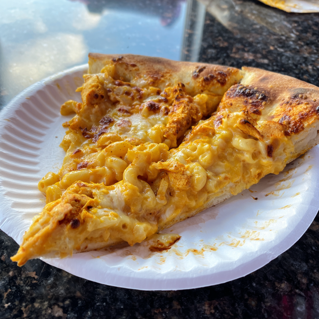 A slice of pizza with macaroni and cheese on a paper plate.
