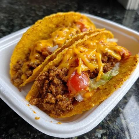 A container of two tacos with cheese and tomatoes.