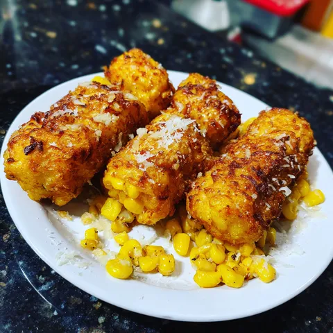 A plate of corn on the cob with cheese on top.