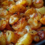 A close-up image of golden-brown, crispy roasted potatoes mixed with sautéed onions and seasoned with herbs.