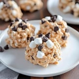 Three sweet, round treats made of marshmallows and chocolate chips are displayed on a white plate.