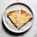 Two slices of cheese pizza on a round plate, resting on a piece of parchment paper.