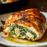 A close-up of a slice of stuffed chicken breast filled with spinach, cheese, and herbs, resting on a plate with a drizzle of sauce.