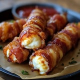 A plate of crispy bacon-wrapped mozzarella sticks served with a side of dipping sauce.