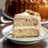 A slice of creamy frosted cake topped with pecans sits on a light green plate, showcasing its layered texture.