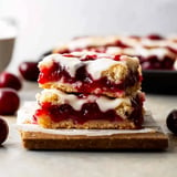 A close-up of two stacked cherry bars with a creamy icing on top, surrounded by fresh cherries.